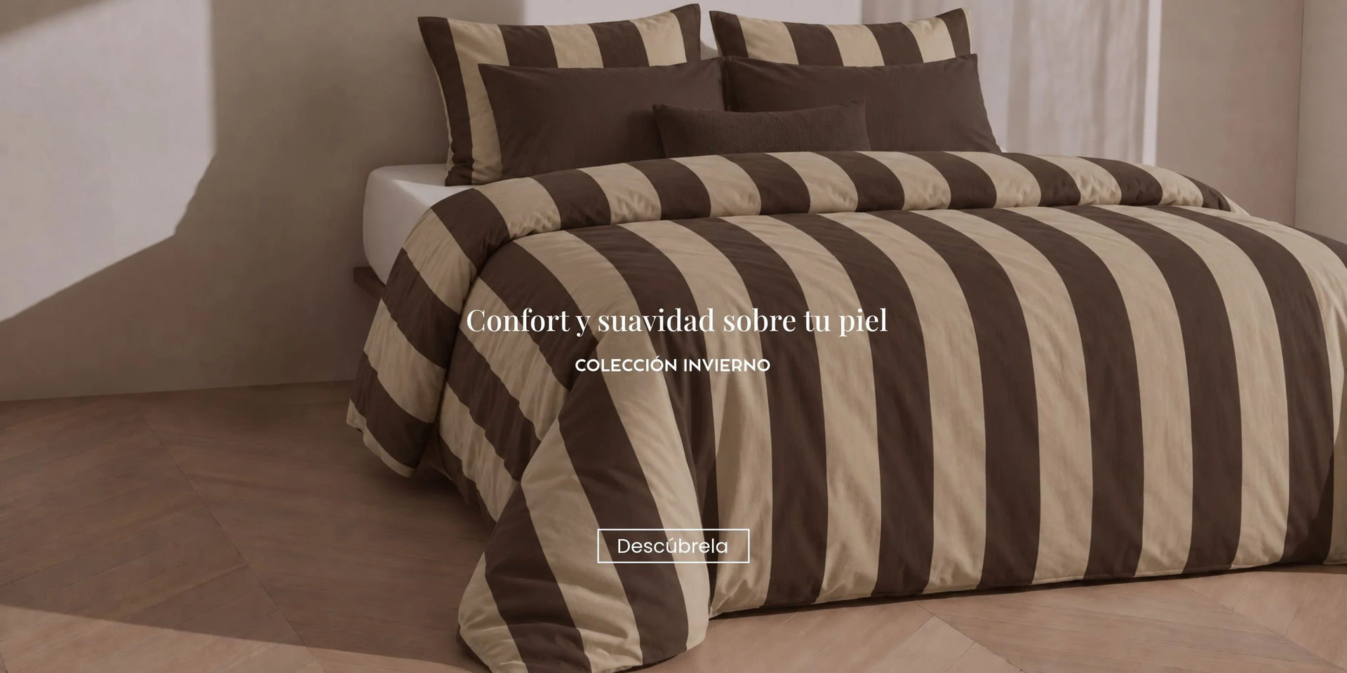Cama vestida con funda nórdica de rayas anchas en tonos marrón chocolate y beige, combinada con cojines a juego en un dormitorio cálido y elegante.