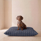 Cama para perro azul marino de cuadros con teckel sentado encima 
